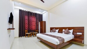 Une chambre d’hôtel dotée d’un grand lit, d’une armoire en bois, d’un téléviseur fixé au mur et d’un coin salon avec des chaises et une petite table.