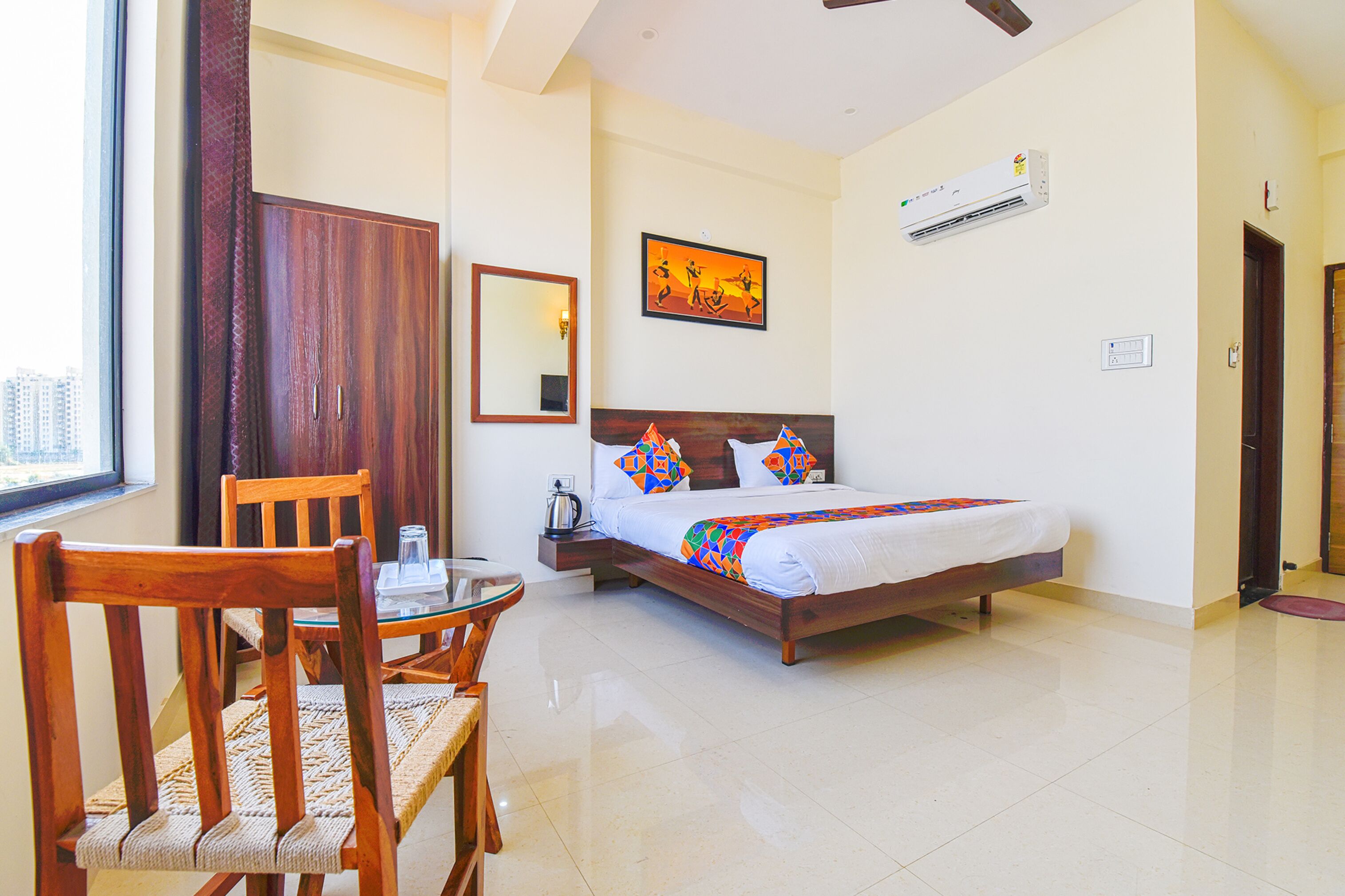 A hotel room with a bed, a wooden chair, a table, a mirror, and a painting on the wall.