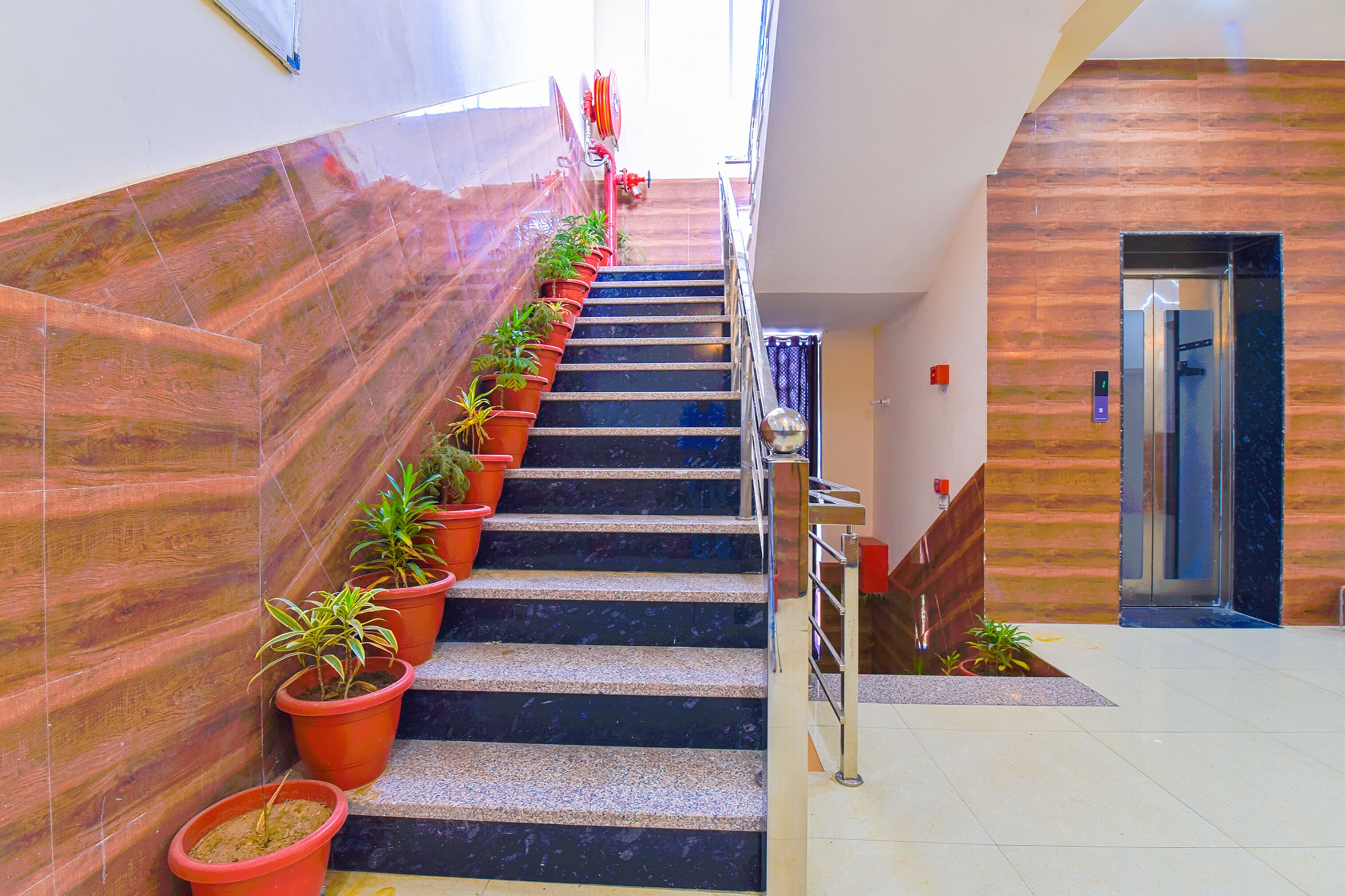 A staircase with potted plants, a handrail, and a modern elevator.