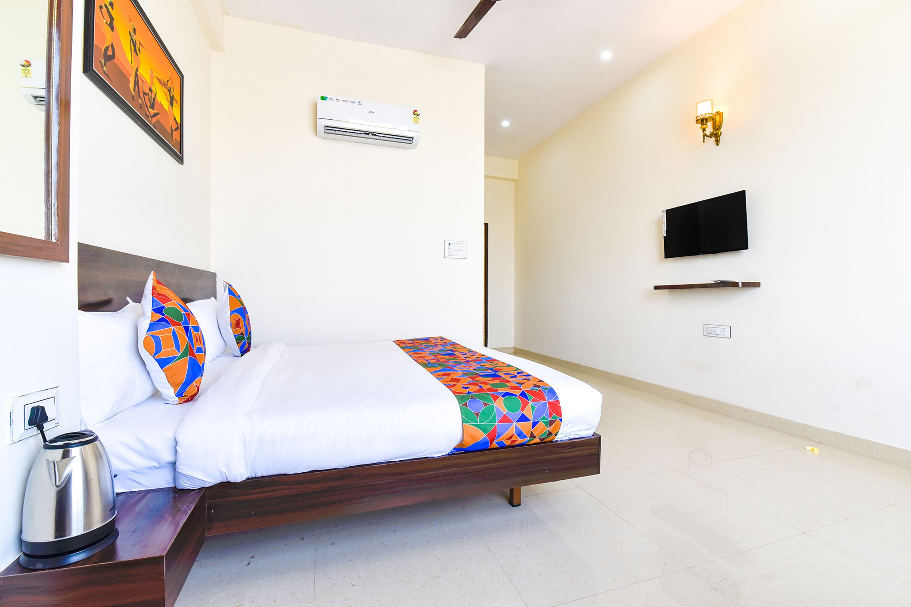 A hotel room with a bed, a coffee maker, an air conditioner, a TV, and a wall-mounted shelf.