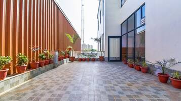 A courtyard with potted plants arranged in rows, a tiled floor, and a modern building with large windows.
