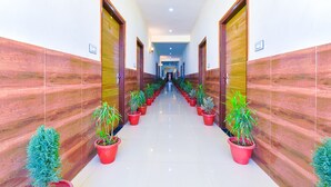 Un couloir aux murs recouverts de carreaux rouges, avec des portes en bois et des plantes en pot.