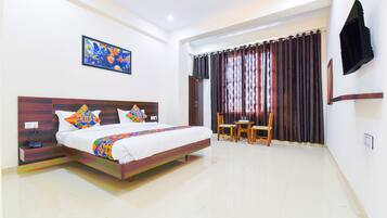 A hotel room with a bed, a desk, a chair, a TV mounted on the wall, and a painting on the wall.