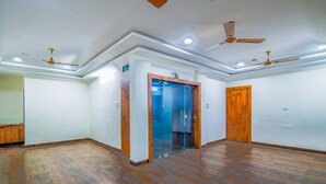 A spacious room with wooden flooring, a glass door entrance, and ceiling fans. - Fabexpress Regal (Indore)