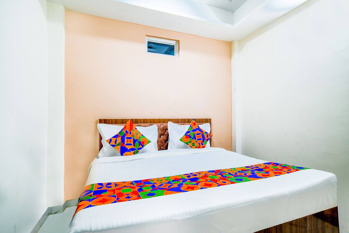 A neatly made bed with a colorful geometric-patterned bedspread, a wooden headboard, and a small window above the bed.