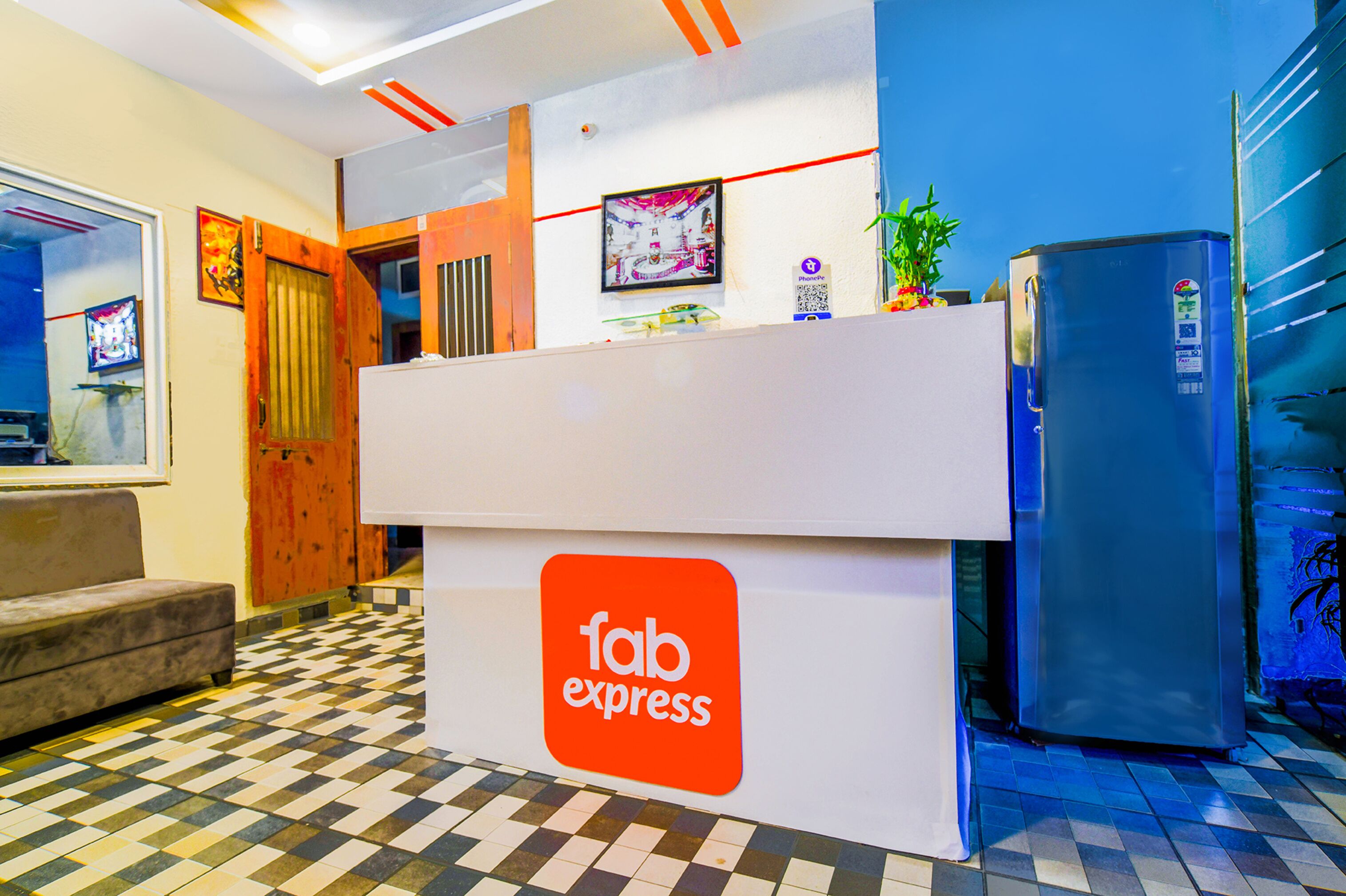 A reception area with a checkered floor, a sofa, a refrigerator, and a wall-mounted screen.
