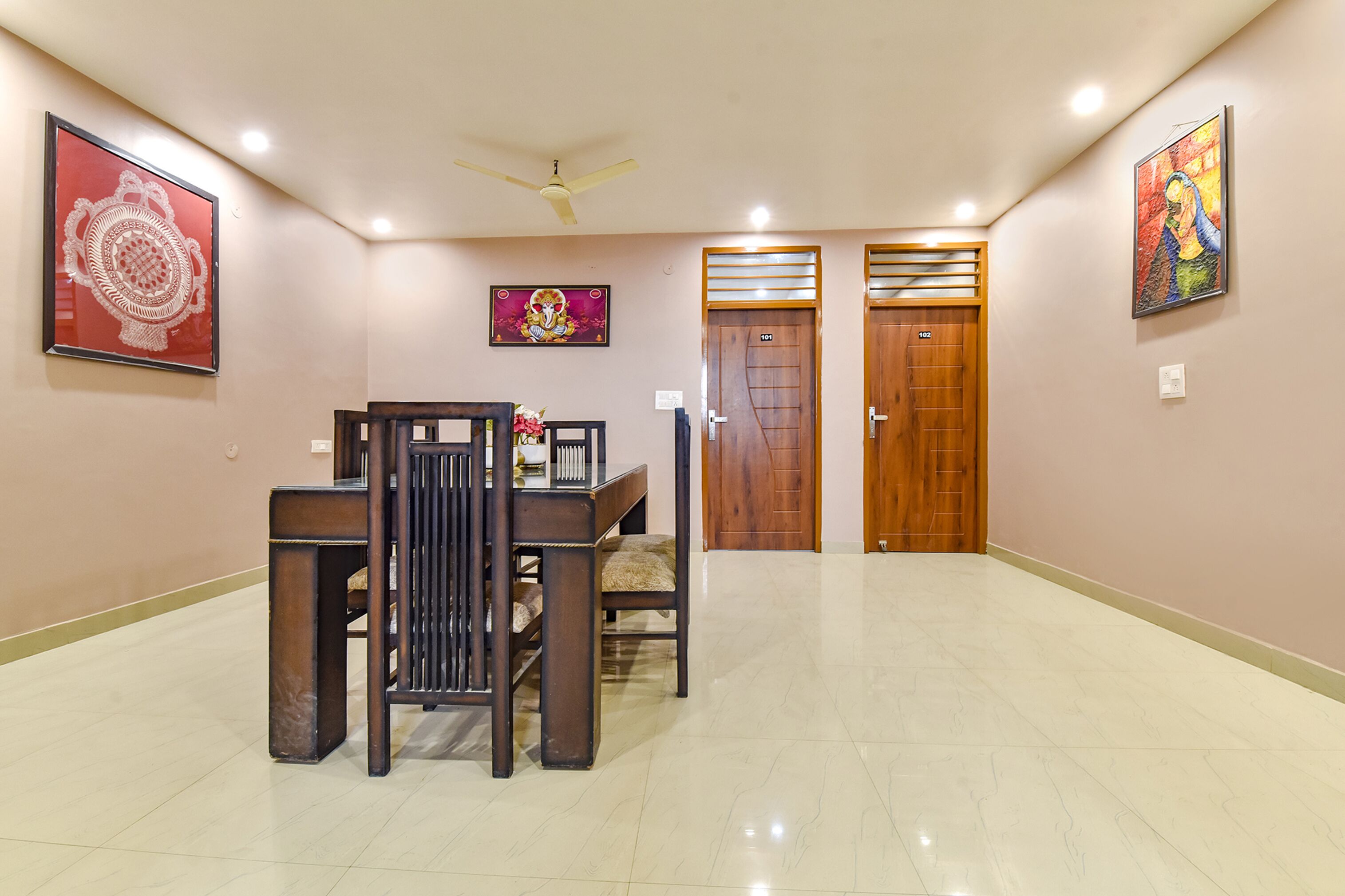 A spacious hallway with a dining area featuring a wooden table and chairs, two wooden doors, and ceiling fans.
