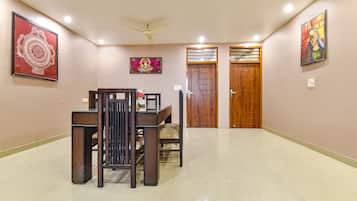 A spacious hallway with a dining area featuring a wooden table and chairs, two wooden doors, and ceiling fans.