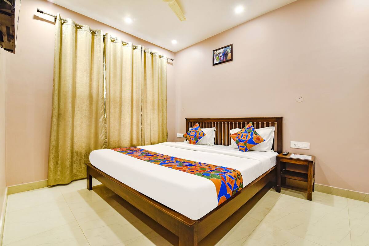 A neatly made bed with a colorful geometric-patterned bedspread, a wooden headboard, and a bedside table with a lamp.
