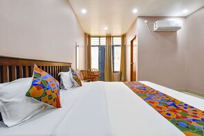Een hotelkamer met een groot bed, een houten hoofdeinde, een kleurrijk kussen, een stoel en een raam met gordijnen.