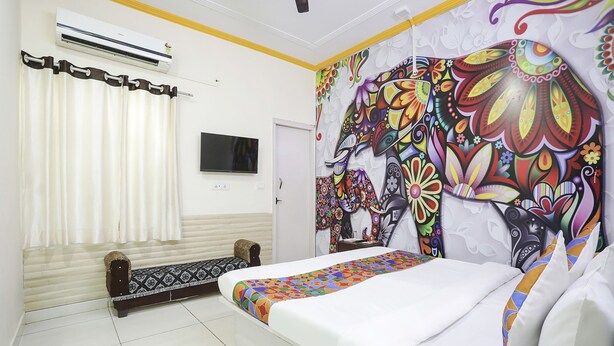 A bedroom with a bed, a TV, an air conditioner, and a colorful mural on the wall. - Fabexpress Grand Resort (Agra)