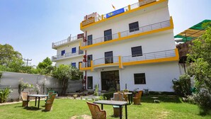 A multi-story hotel with a balcony, outdoor seating area, and a well-maintained garden. - Fabexpress Grand Resort (Agra)