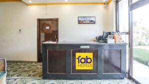 A reception desk with a 'fab hotels' sign, a door, and a window with a view of greenery. - Fabexpress Grand Resort (Agra)