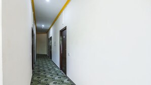 A narrow hallway with patterned floor tiles, white walls, and doors on both sides. - Fabexpress Grand Resort (Agra)