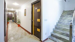 A hallway with a marble floor, a staircase with a metal railing, and doors with yellow accents. - Fabhotel Br International (Agra)