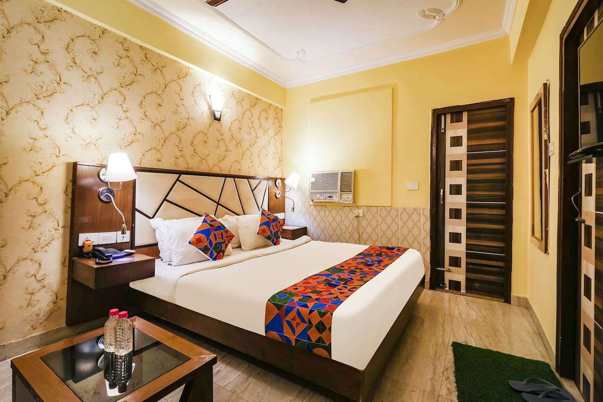 A hotel room with a bed, bedside tables, a nightstand, a lamp, a wall-mounted air conditioner, and a door with a striped pattern.