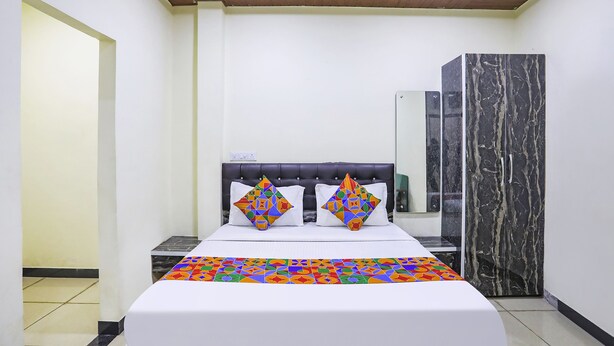 Un dormitorio con una cama, dos almohadillas decorativas, una mesita de noche, un armario y una lámpara en el techo.