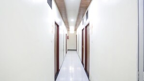 Un pasillo largo y estrecho con paredes blancas y suelo de baldosas, que conduce a una puerta al final.
