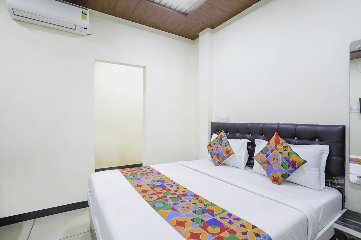 A hotel room with a bed, a headboard, a bedside table, and an air conditioning unit.