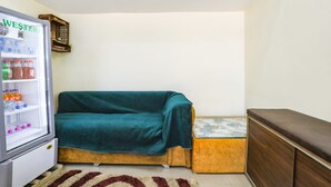 Una habitación pequeña con sofá cama, un refrigerador compacto y un armario de madera.