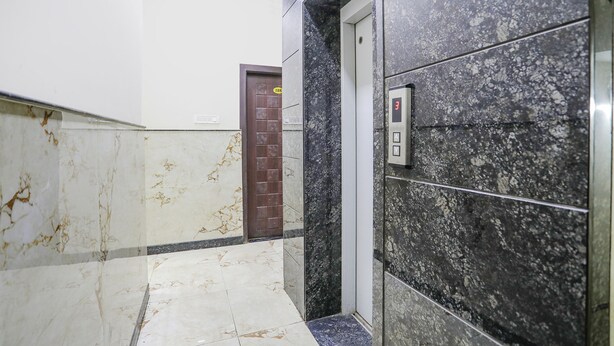 Un passadís amb sòls de marbre, una porta marró i un panell de control d'ascensor fixat a la paret.
