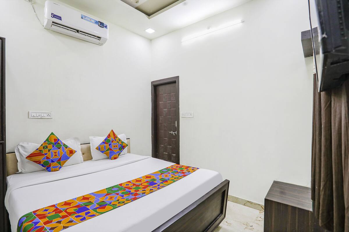 A hotel room with a bed, a TV, an air conditioner, and a door.