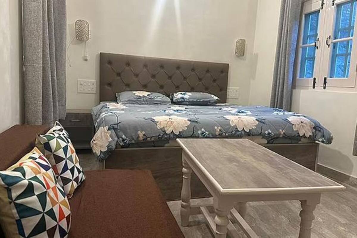Quarto com cama, mesa de madeira, sofá e janela com cortinas.