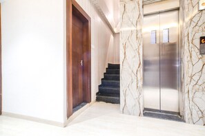 A marble-floored hallway with a wooden door and a staircase leading to an elevator. - Fabhotel Awadhvue (Indore)