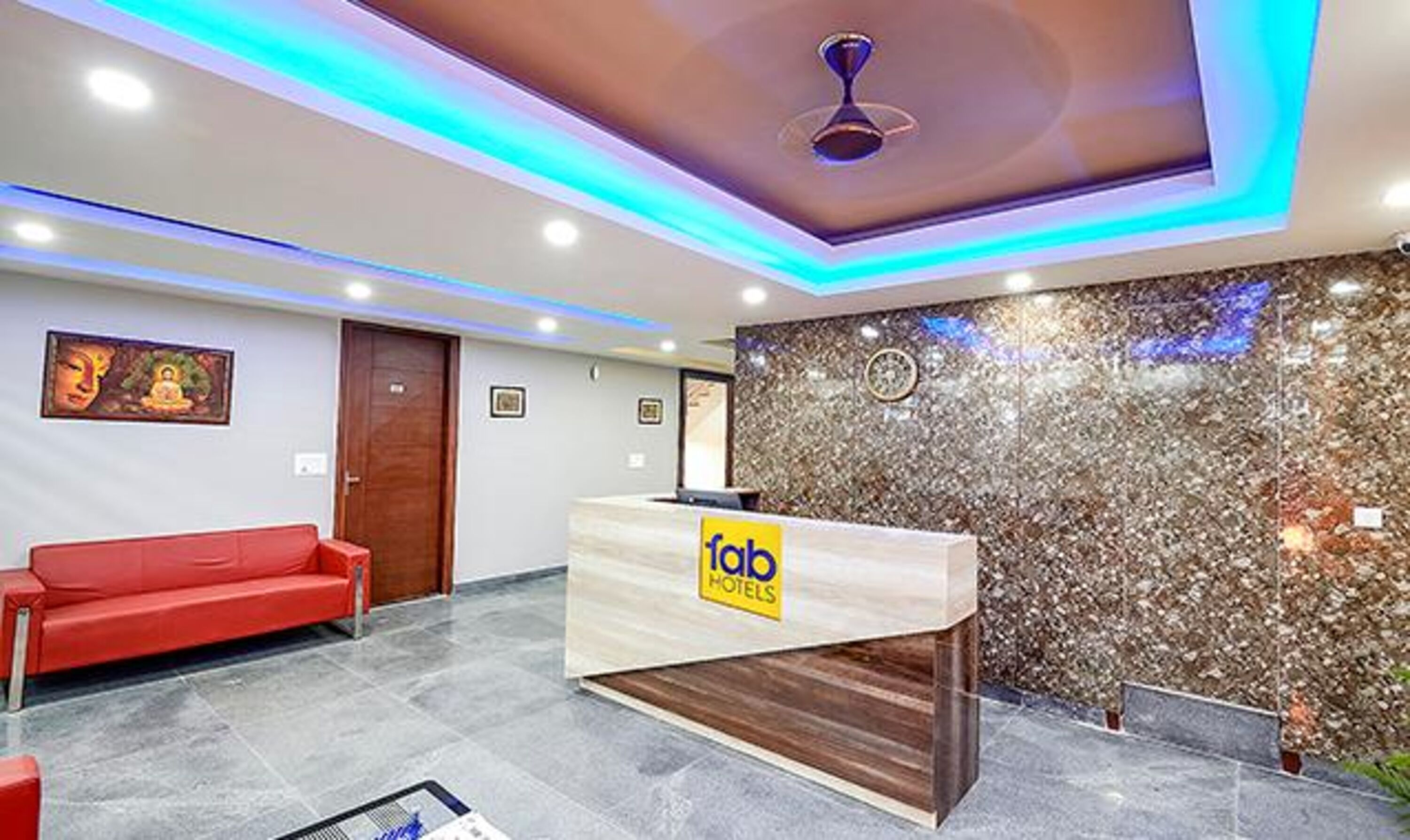A hotel reception area with a red sofa, a wooden reception desk, and a decorative wall with a clock.
