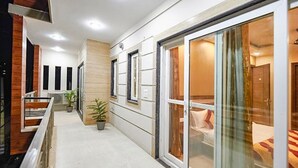 A hallway with a wooden floor, potted plants, and a glass door leading to a room with a bed. - Fabhotel Indian (Gurugram)