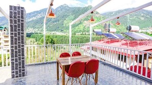 A balcony with a table and chairs, a stone wall, and a view of mountains and solar panels. - Fabhotel Outhills (Manali)