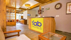 A reception area with a wooden reception desk, a glass table, and a reception sign. - Fabhotel Outhills (Manali)