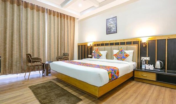 Une chambre d’hôtel avec un grand lit, deux chaises, une petite table et une table de chevet avec une bouilloire.