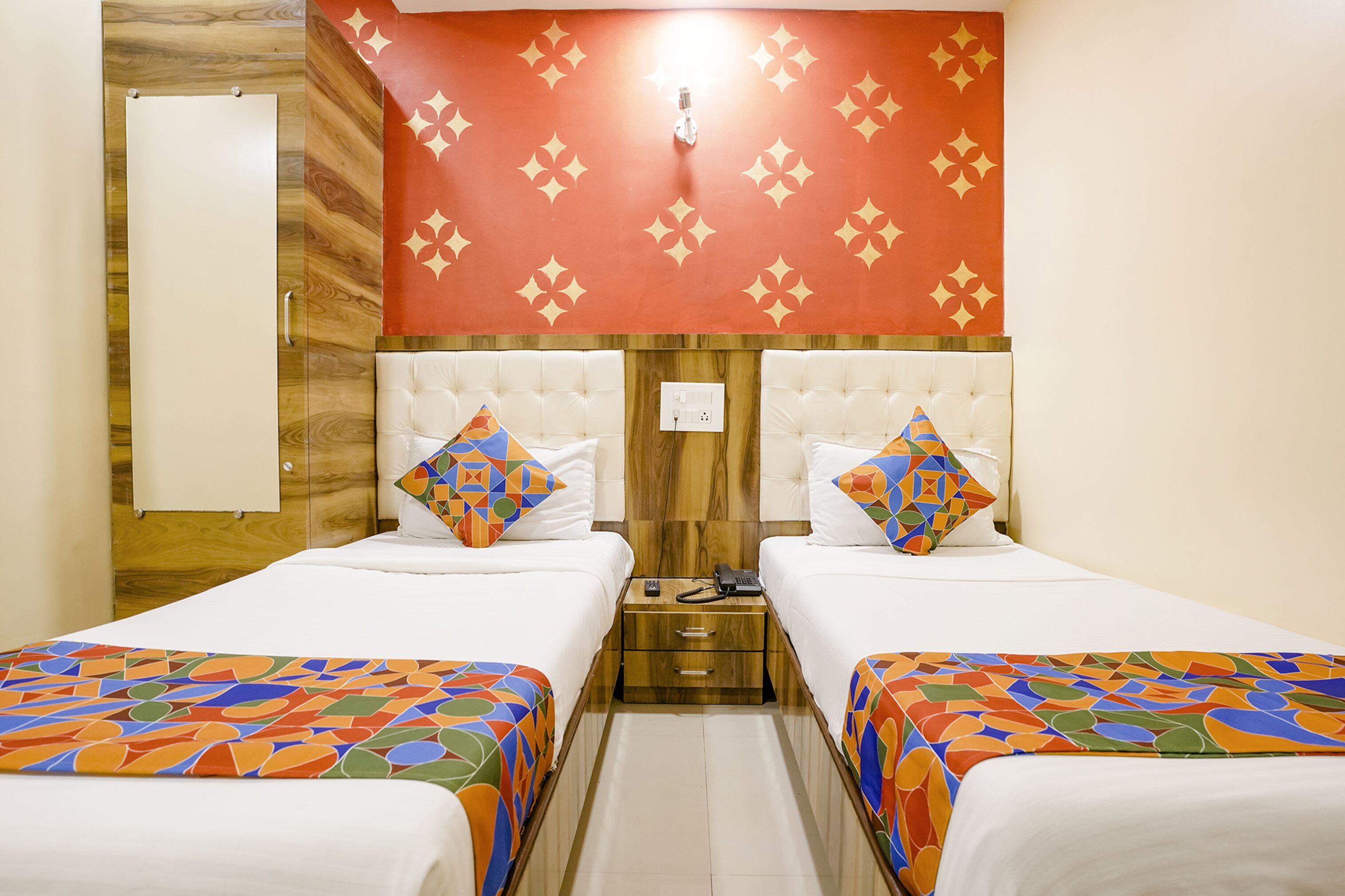 A hotel room with two beds, each with a colorful geometric-patterned bedspread, a wooden headboard, and a red wall with a star pattern.