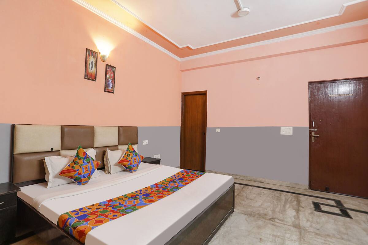 A hotel room with a bed, a nightstand, a wall-mounted lamp, and a door.