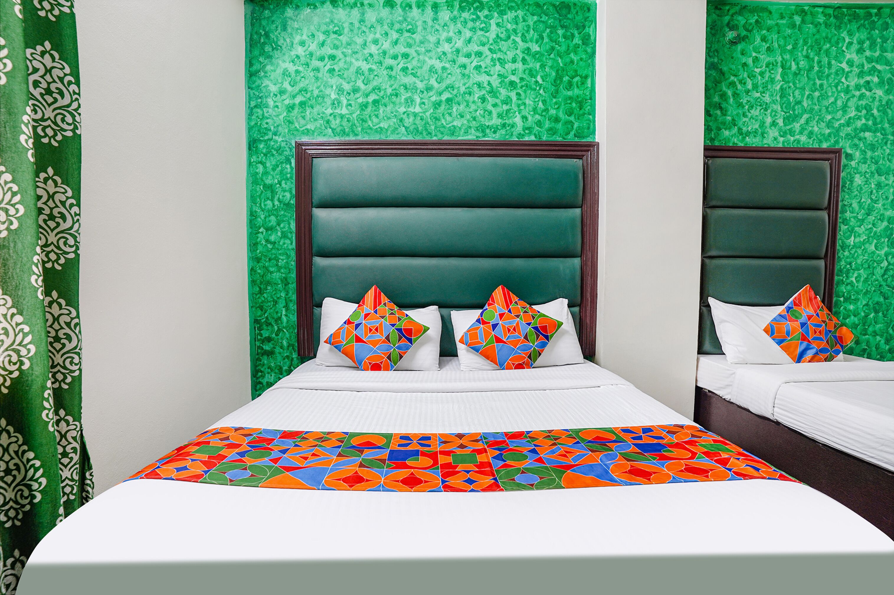 A hotel room with a large bed, two pillows with a geometric pattern, and a colorful bedspread.