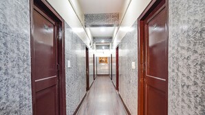 A hallway with marble walls and wooden doors, leading to a room with a framed picture on the wall. - FabHotel Pavithraa Edition (Bengaluru)