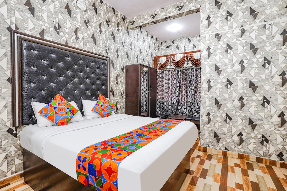 Un dormitorio con una cama grande, cabecera capitonada, papel tapiz estampado y suelo de madera.