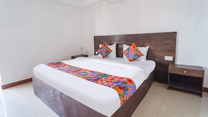 A neatly made bed with a colorful blanket, a wooden headboard, and two bedside tables with drawers. - FabExpress California Inn (Kodaikanal)