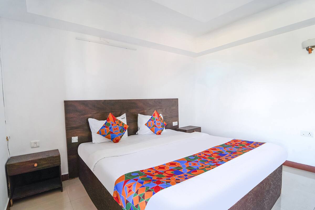 A hotel room with a large bed, two nightstands, a wooden headboard, and a colorful throw blanket.