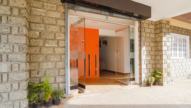 A modern building entrance with a glass door, stone walls, and potted plants. - FabExpress California Inn (Kodaikanal)
