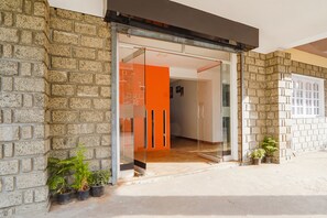 A modern building entrance with a glass door, stone walls, and potted plants. - FabExpress California Inn (Kodaikanal)