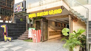 The exterior of a hotel named "Hotel Season Grand" with a checkered floor pattern, a signboard, and a "Pop Corn" snack stand. - Fabhotel Season Grand (New Delhi)