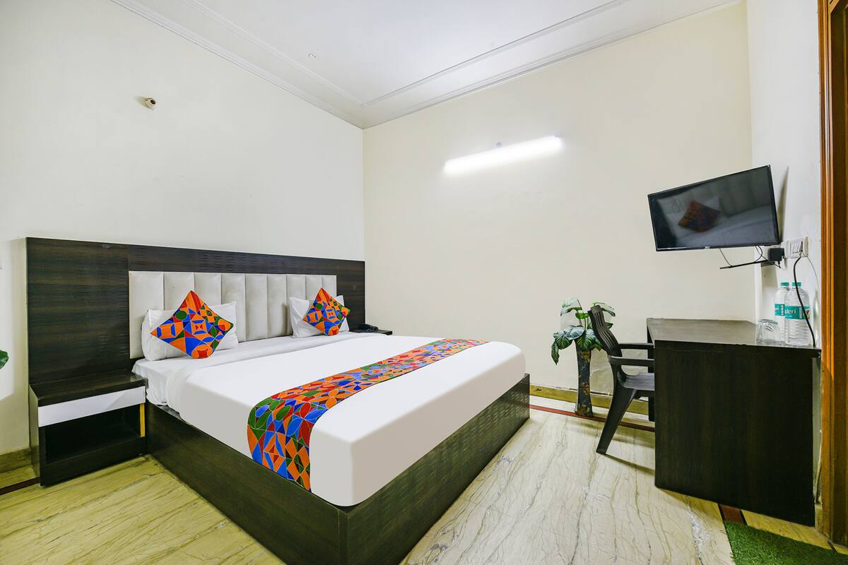 Una habitación de hotel con cama, escritorio, silla, televisor y planta.