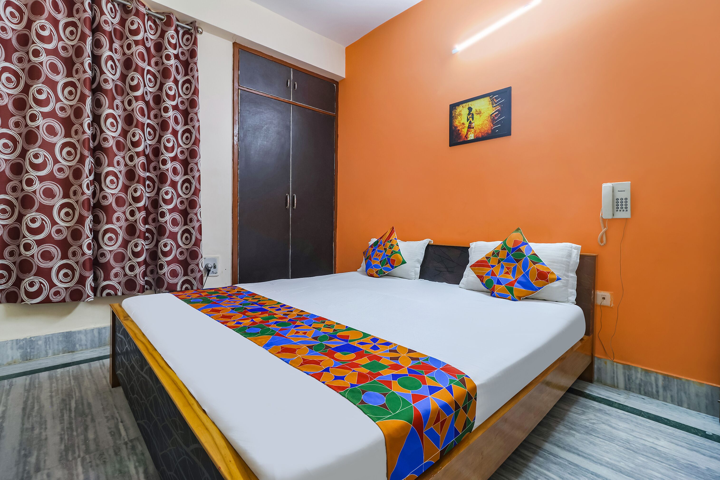 A bedroom with a bed, orange walls, a patterned curtain, and a painting on the wall.