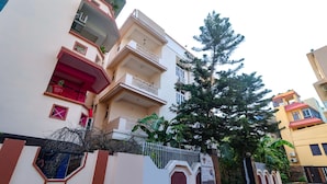 Un hotel de diversos pisos amb balcons, una entrada tancada i un arbre gran al davant.