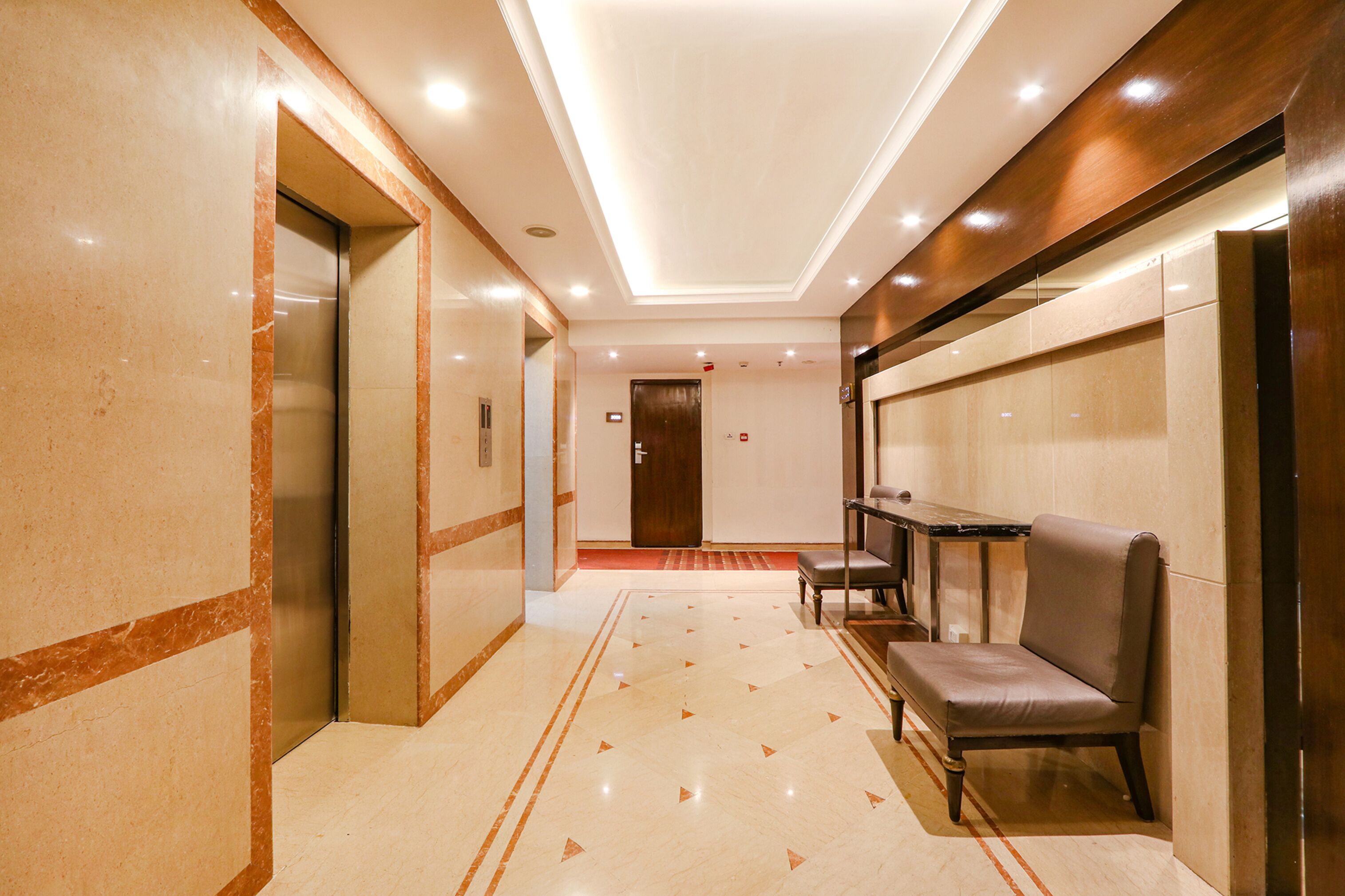 A hotel corridor with a marble floor, a bench, and a door at the end.