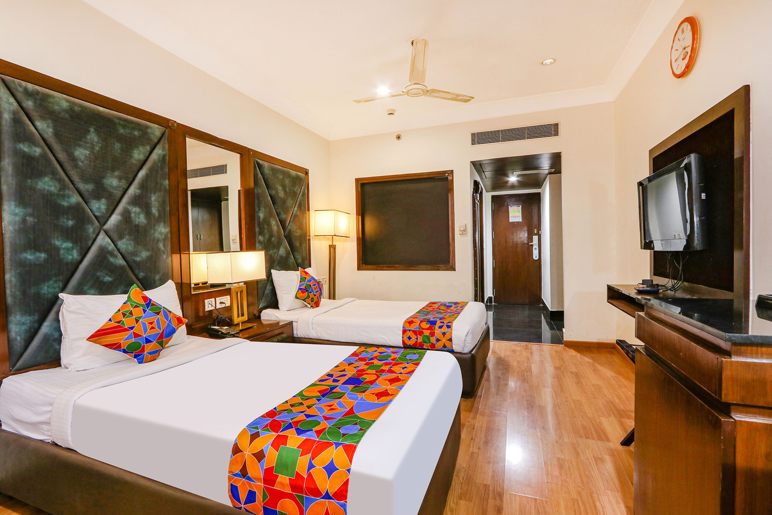 A hotel room with two beds, a television, a desk, and a mirror.