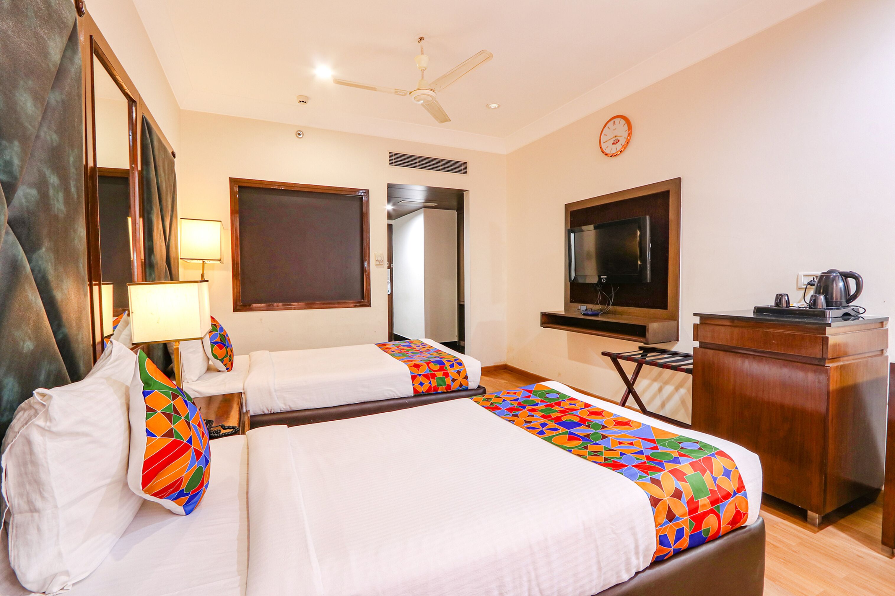 A hotel room with two beds, a desk, a television, and a clock on the wall.