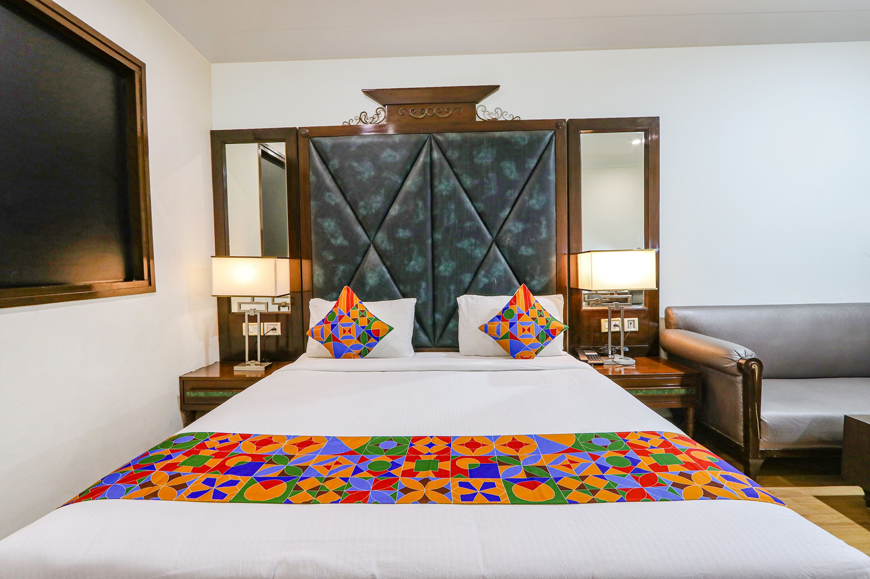 A hotel room with a large bed, two bedside tables with lamps, a sofa, and a decorative headboard.